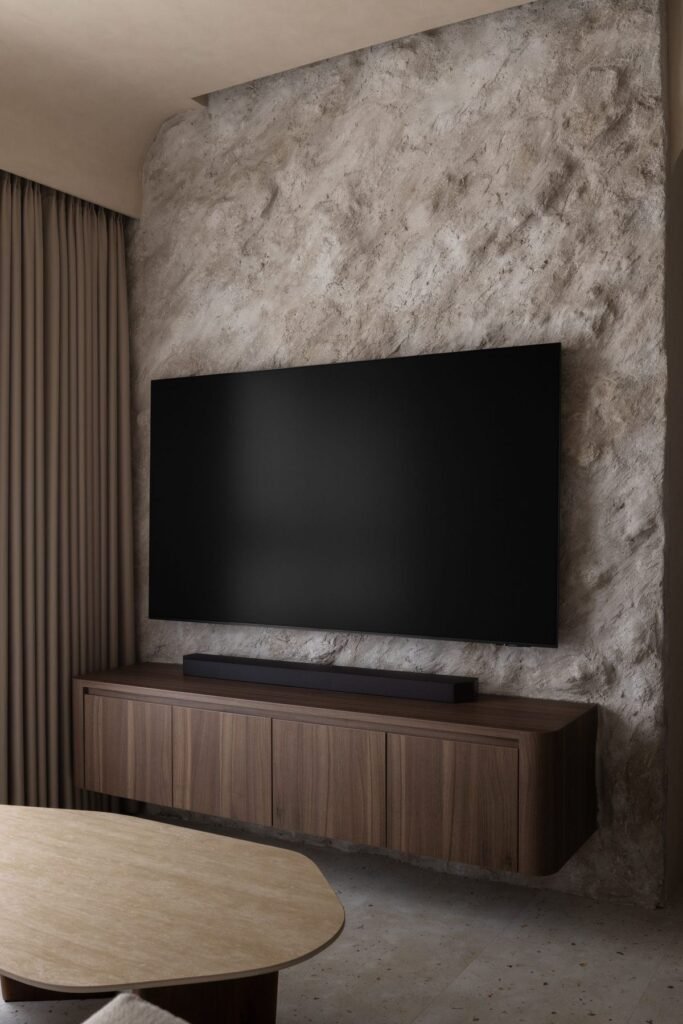 Stone feature wall behind the TV with a floating walnut-tone console